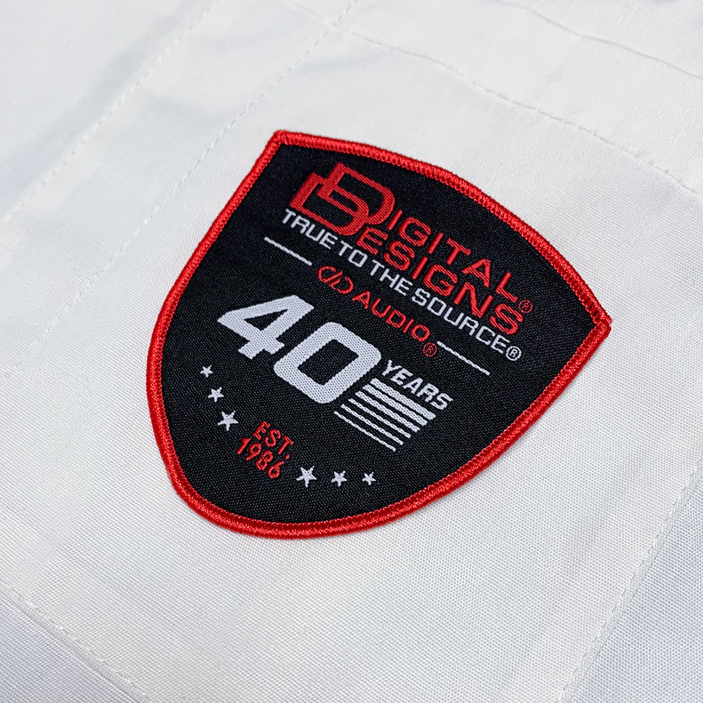 DD 40th Anniversary Woven Patches - photo of digital designs patch adhered to twill white fabric  - Patch contains classic Digital Designs style logo, True to the Source slogan, modern DD AUDIO logo, 40 Years design and EST 1986 with starts and bars